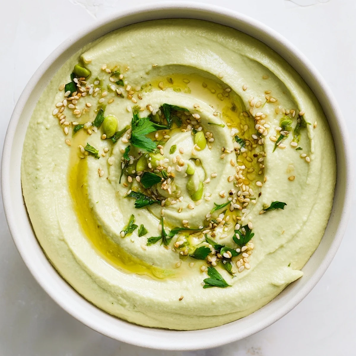Creamy green Edamame Hummus swirled with olive oil in a rustic bowl, with lemon wedges and pita ready for dipping.  