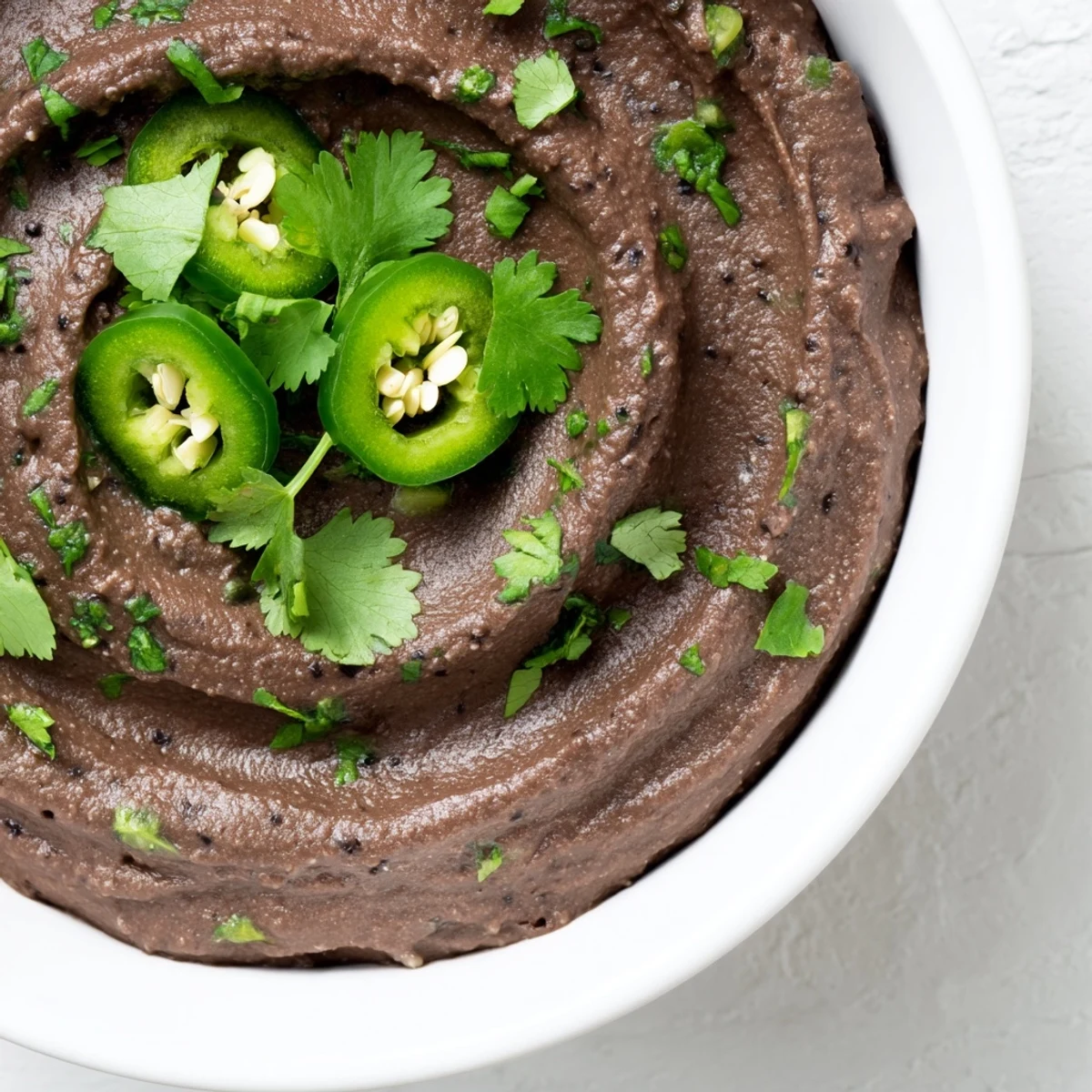 Creamy Spicy Black Bean Dip in a bowl, topped with fresh cilantro and jalapeño slices, served with crunchy tortilla chips.