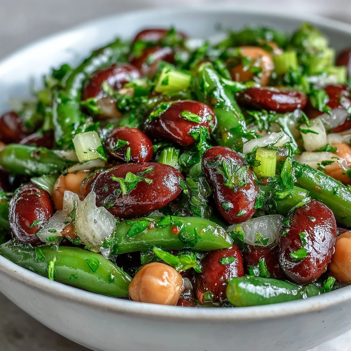 A vibrant Three-Bean Salad with chickpeas, kidney beans, and green beans in a glistening apple cider vinaigrette, served in a white bowl.  