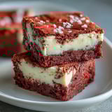 Sliced Red Velvet Cheesecake Brownies reveal fudgy red layers and creamy, rich cheesecake swirls on a plate.