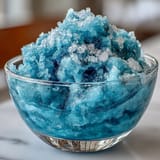 A frosty Blue Raspberry Lemonade Slushie with a sugared rim, blending tangy lemon and sweet blue raspberry flavors for a refreshing treat.