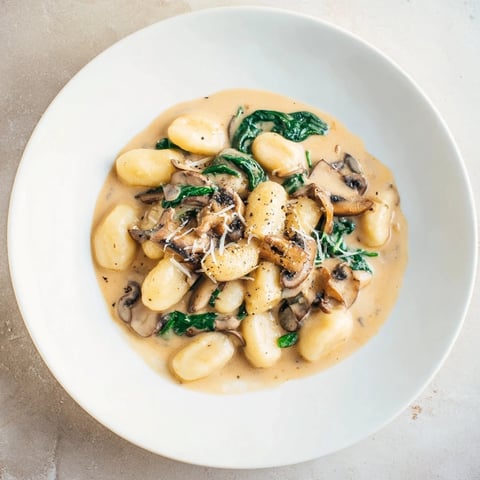Golden, creamy One-Dish Creamy Mushroom and Spinach Gnocchi, fresh spinach and Parmesan cheese topped.