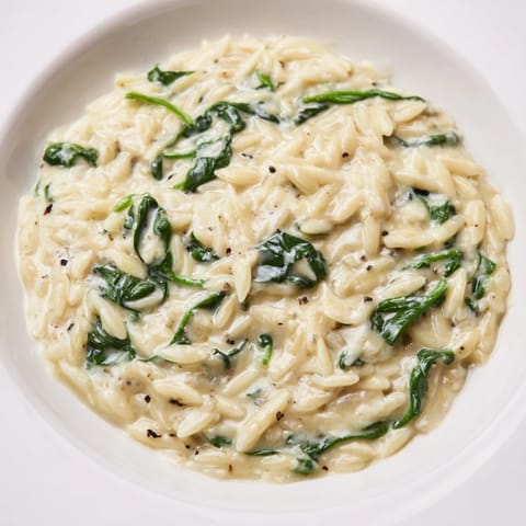 A close-up of creamy spinach orzo, showing the tender pasta and fresh, vibrant spinach leaves.