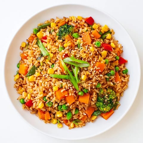 Top-down view of vegetarian vegetable fried rice topped with green onions and sesame seeds, served in a white bowl.