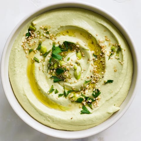 Creamy green Edamame Hummus swirled with olive oil in a rustic bowl, with lemon wedges and pita ready for dipping.  
