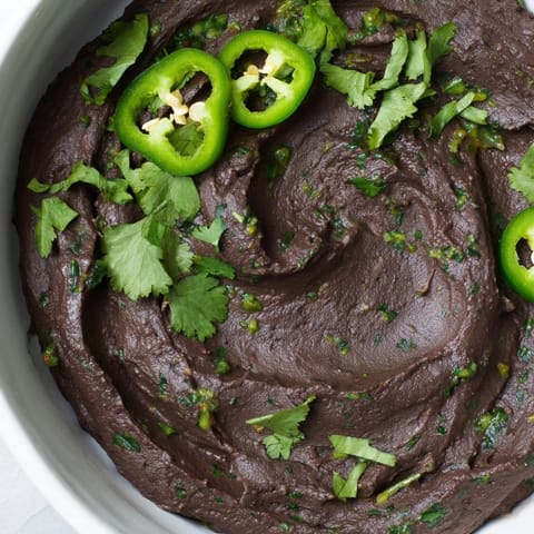 A bowl of Spicy Black Bean Dip garnished with cotija cheese and lime wedges, perfect for party snacking.