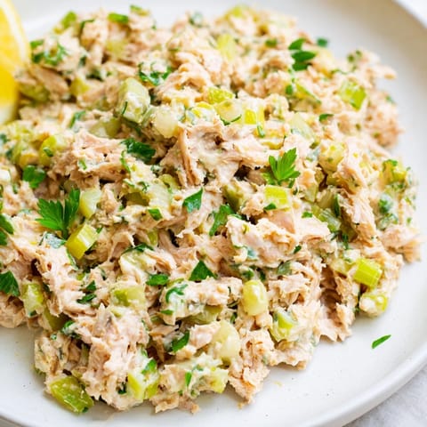 Flaked tuna tossed in spicy Sriracha mayo, garnished with parsley and lemon wedges on a rustic wooden serving board.