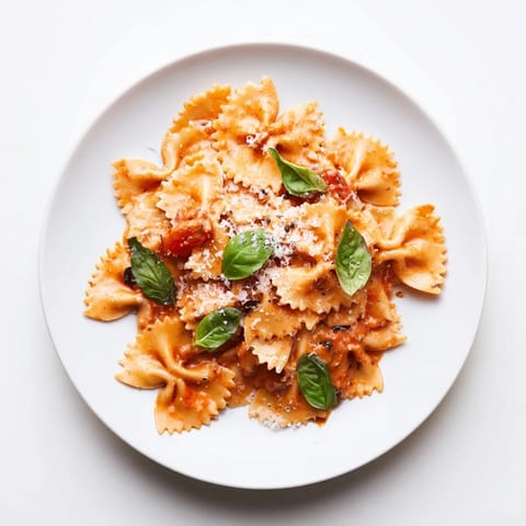 Steaming Tomato Basil Bowtie Pasta in a skillet, topped with extra grated Parmesan cheese and a drizzle of olive oil.  