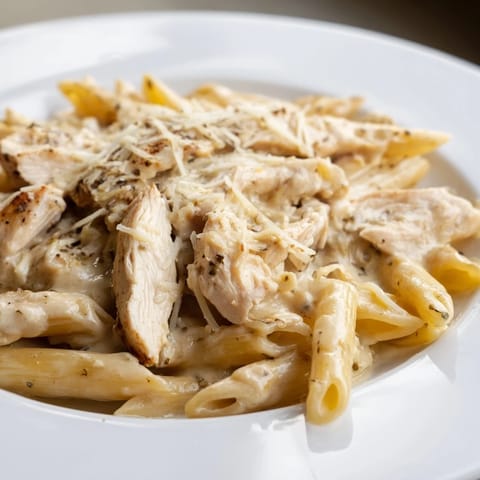 A close-up of Roasted Garlic Chicken Penne with golden chicken, al dente pasta, and melted Parmesan in a velvety sauce.  