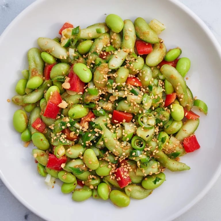 Chilled edamame salad with red bell pepper, visible sesame seeds, awaiting a delicious bite.